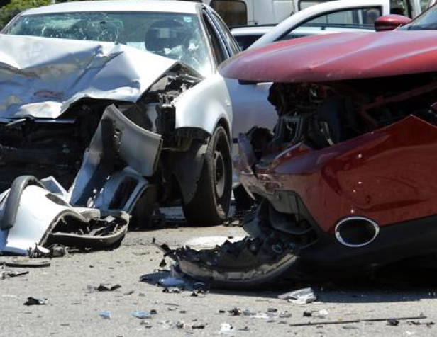 Two heavily damaged cars, one silver and one red, after a collision on a road with debris scattered around.