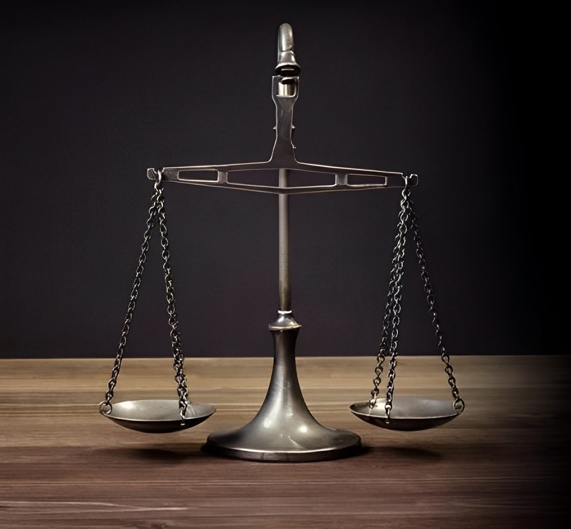 A metal balance scale with two hanging pans on a wooden surface, against a dark background.