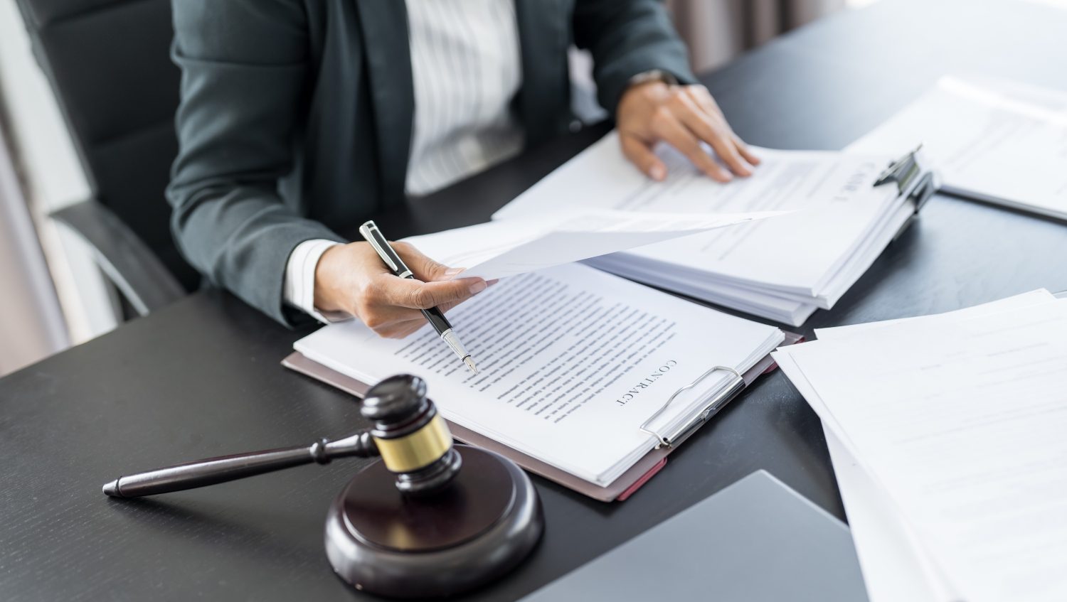 A person in a suit reviews and signs legal documents at a desk with a gavel and clipboard.